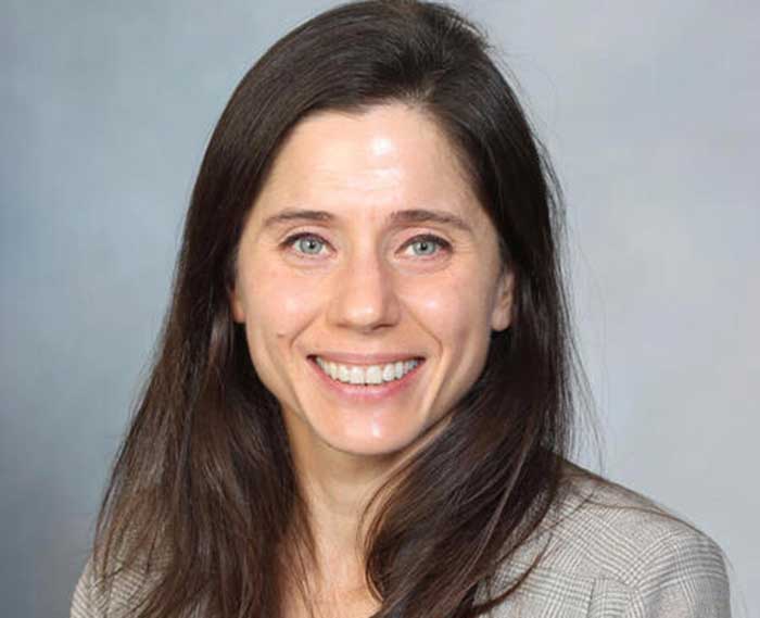 Individual in front of gray background smiling at camera