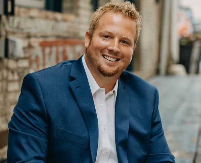 Individual wearing blue blazer seated in front of what appears to be a brick wall