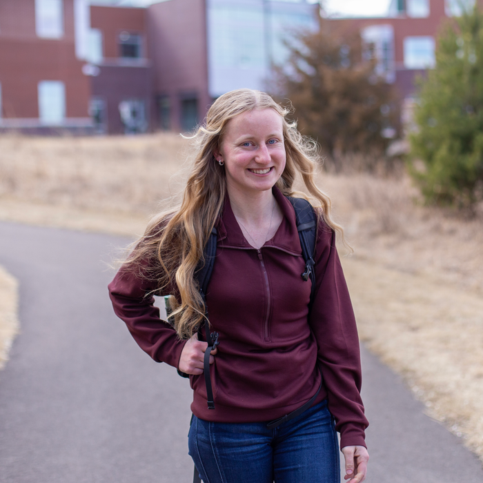 girl walking in front of a building wearing a backpack smiling at the camera