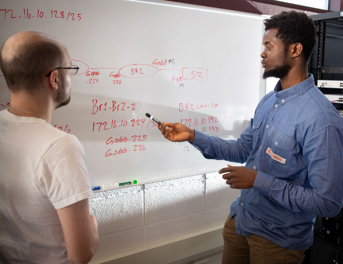 Students reviewing network diagrams and IP addressing on a classroom whiteboard