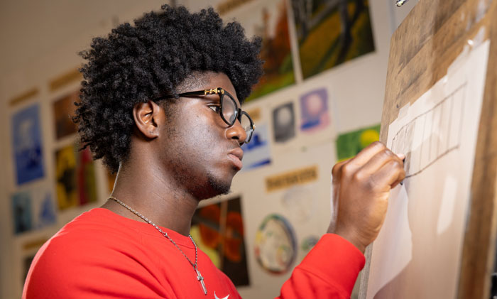 Art student sketches on a large drawing surface in a studio classroom