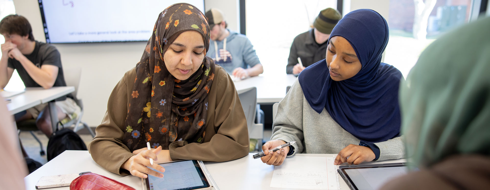 two students in classroom working at table with tablets