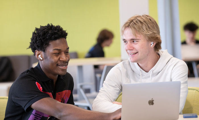 Two students working together on a laptop in a campus study area.