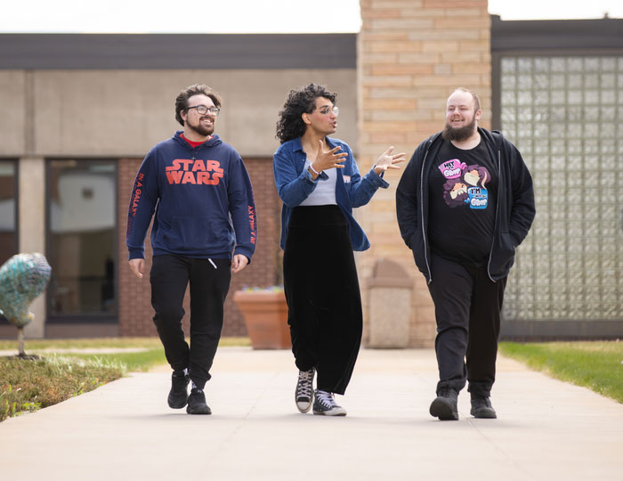 Three students walking together on a college campus walkway between academic buildings
