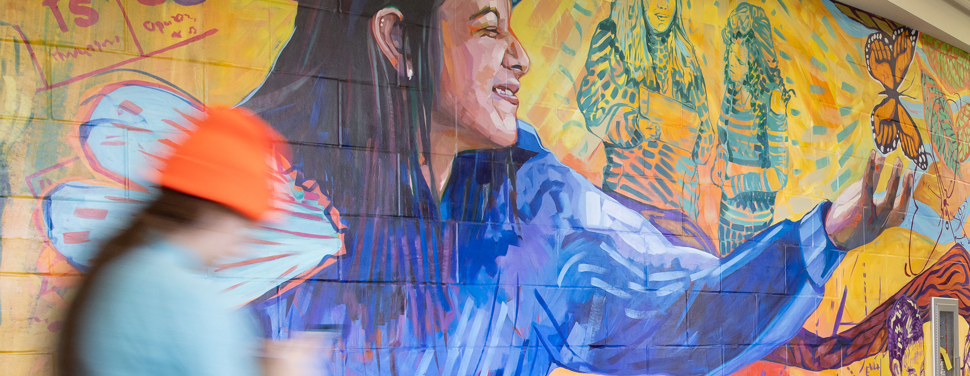 colorful mural on brick wall in hallway with blurry person in the foreground walking by