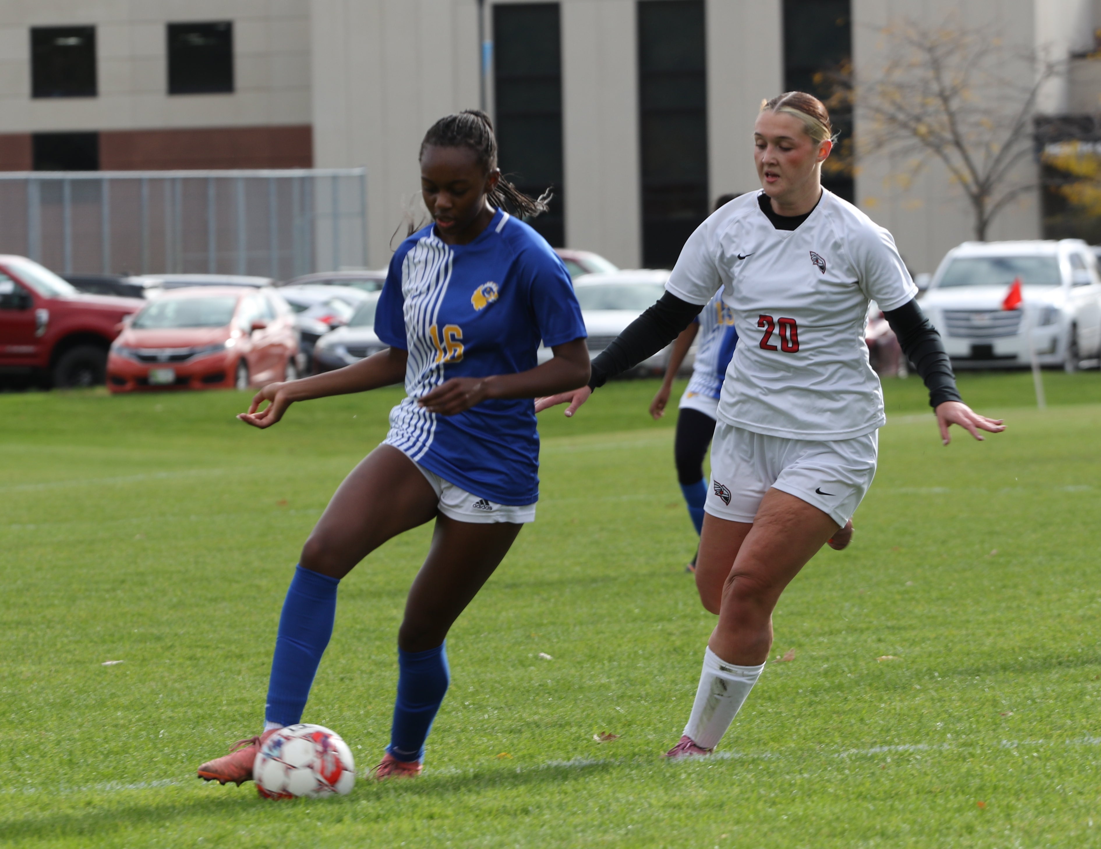 Two women actively playing soccer outside on the field. One women has the ball while the other is trying to get the ball away from her.