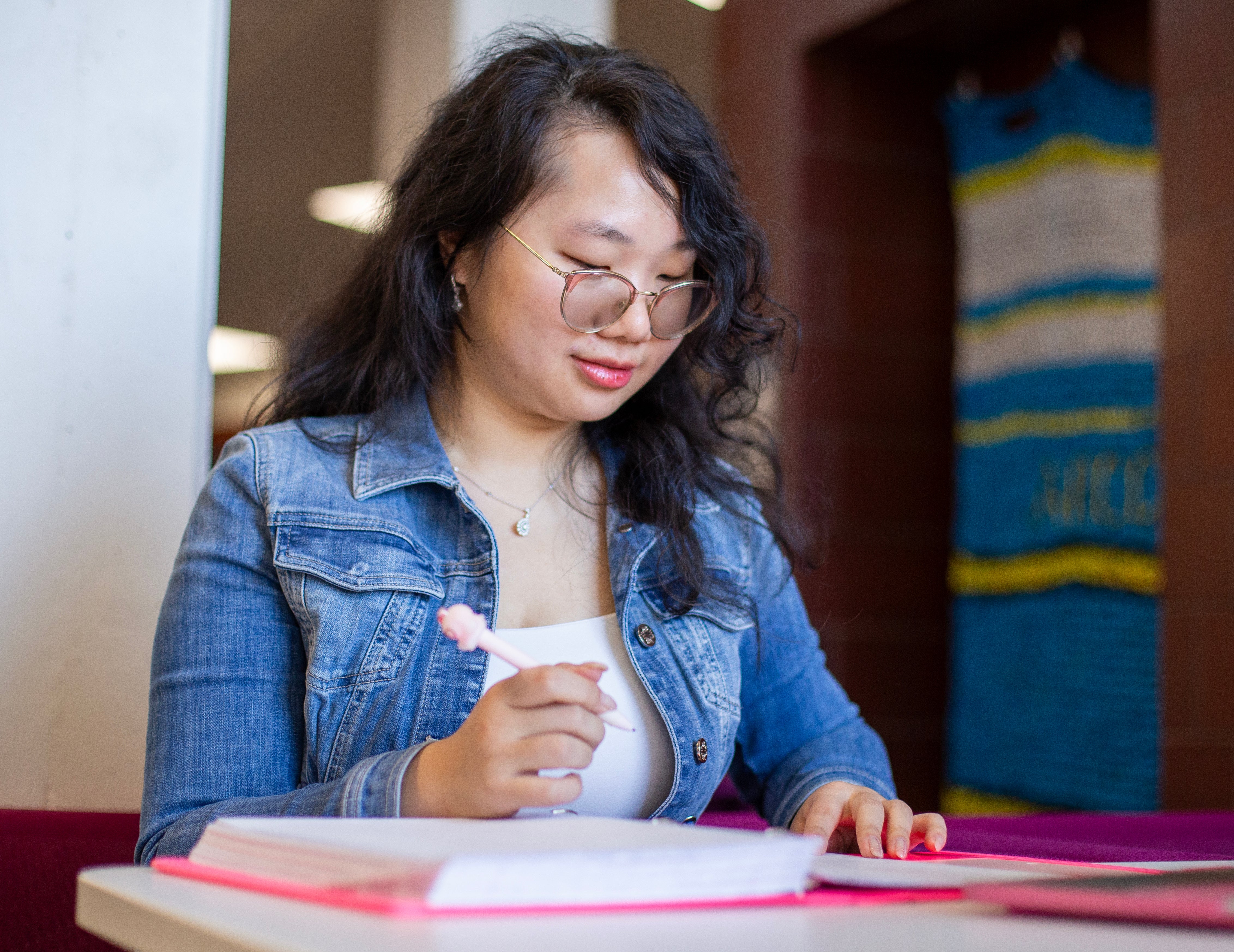A women sitting at a desk looking down at her binder filled with papers. She has a pencil in her hand. 