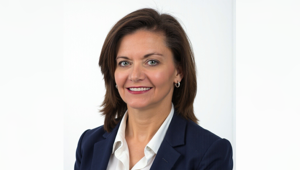 Portrait of a professionally dressed individual with short hair, smiling at the camera against a plain white background.