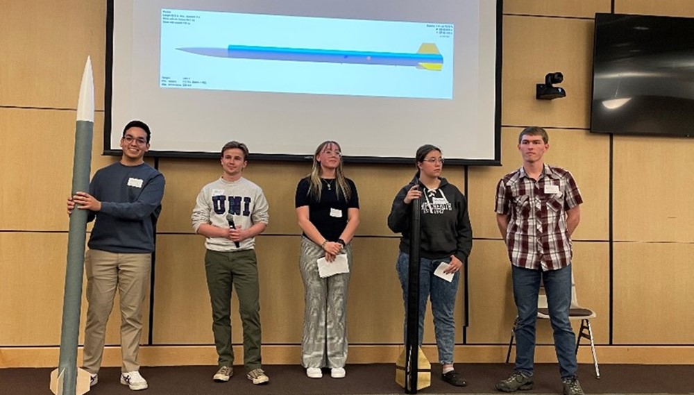 Five students stand in front of a presentation screen.